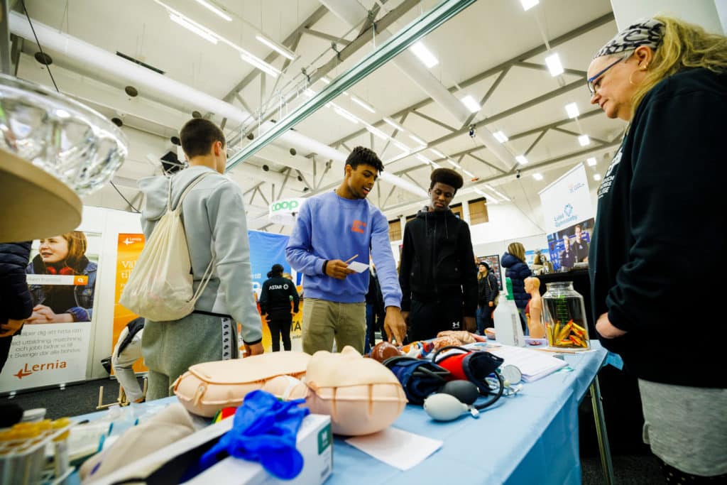 Three young men in front of a table with health education equipment such as models of organs, an exercise dummy and blood pressure monitors.