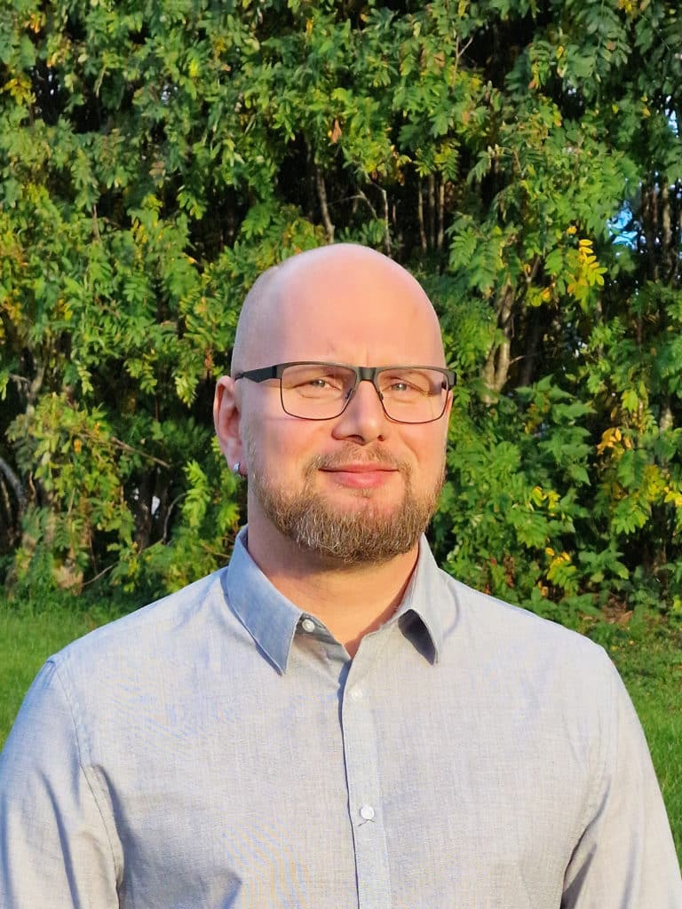 Johan Larsson, projektledare för entreprenörsboende vid Bodens kommun, står framför en grönskande buske och ser glad ut. 