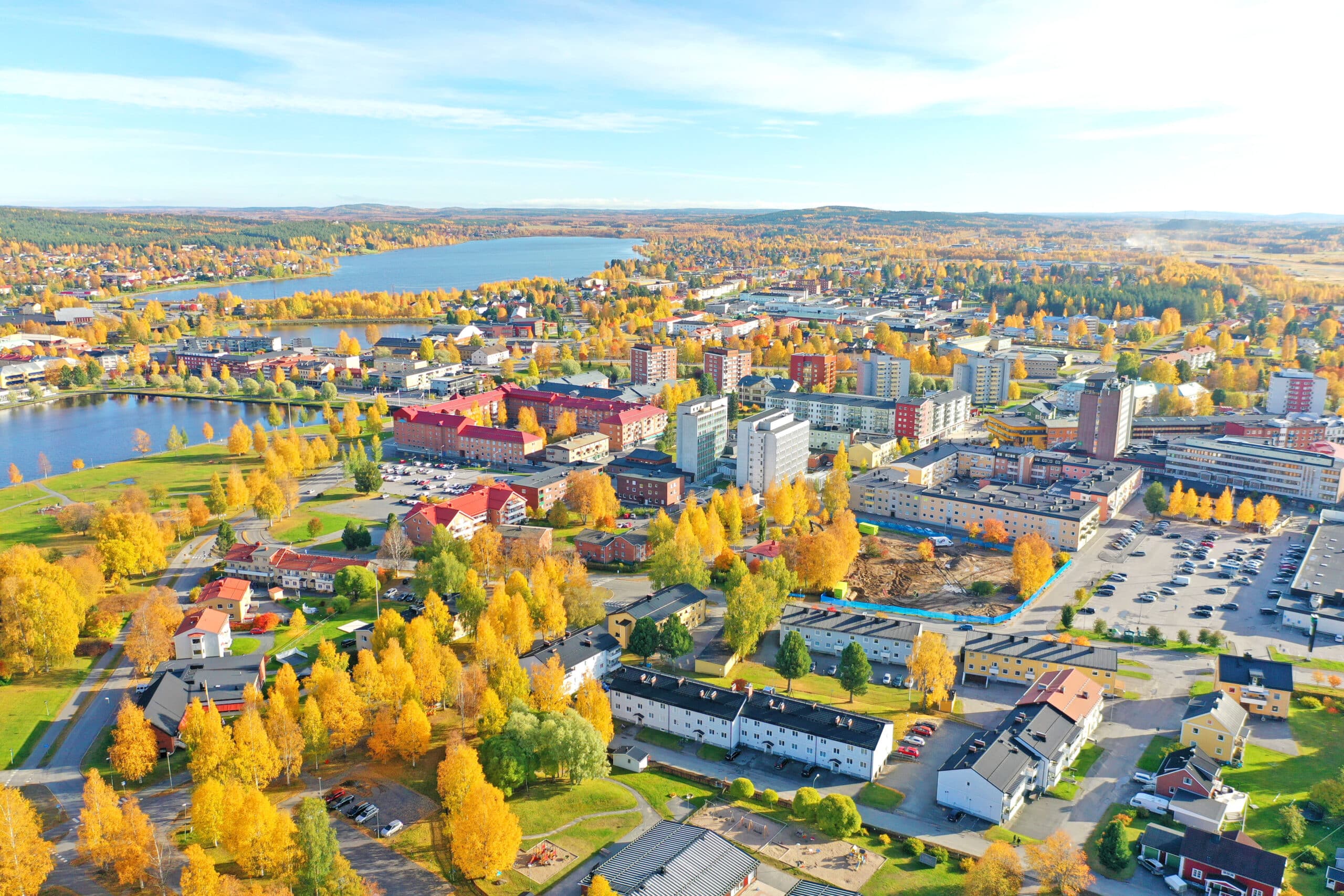 Drönarbild över Boden centrum. Himlen är blå och lövträden har blivit gula. Gräset är grönt och det syns både en sjö och flera byggnader.