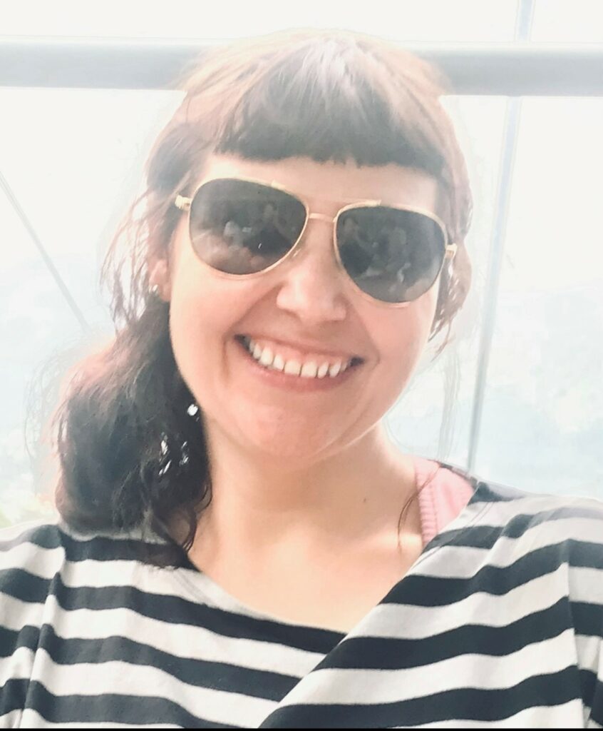 Smiling woman with sunglasses and striped sweater, posing in front of a window.
