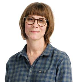 Portrait of a woman with short brown hair, glasses and a blue and green plaid shirt, smiling at the camera.