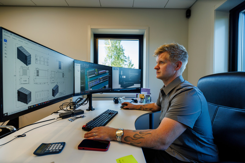 Person working at a multi-screen computer displaying technical drawings and design work.