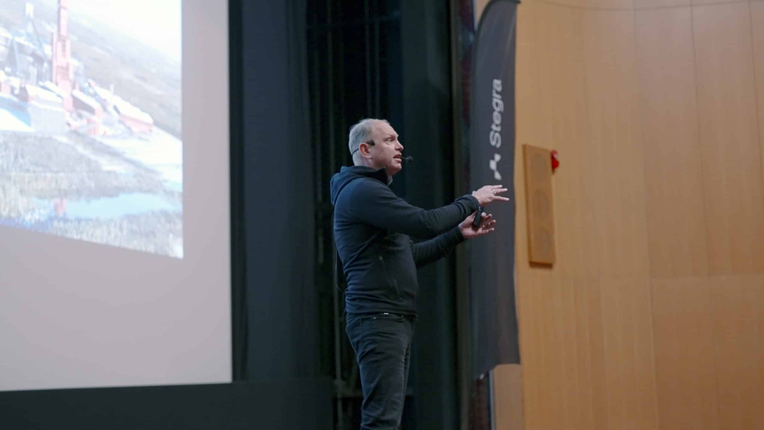 Henrik Henriksson, vd för Stegra, talar inför en publik på Folkets Hus i Boden. I bakgrunden syns en projektion av det gröna stålverket som byggs på Boden Industrial Park.