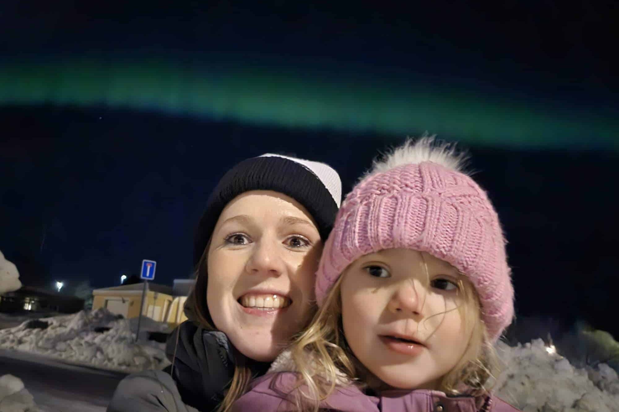 Two people, an adult and a child, with the Northern Lights in the background