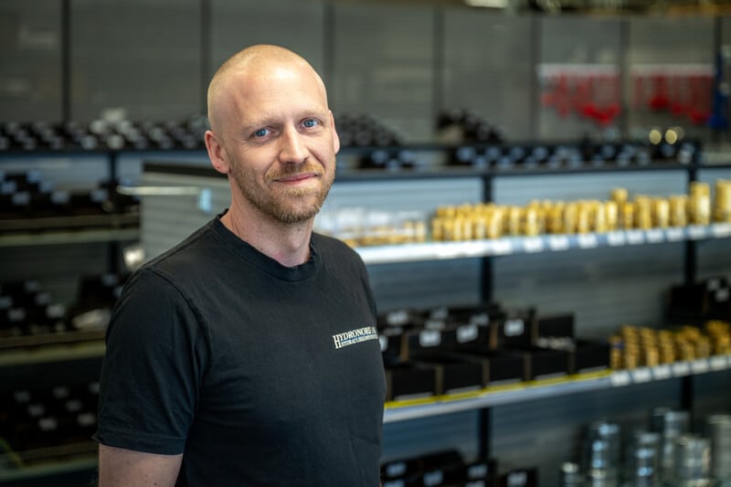 Alf Bernedal, vd för Hydronord, står i butiksmiljö framför hyllor fyllda med hydraulikdelar och kopplingar.
