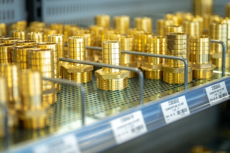 Mässingsfärgade kopplingar och slangdelar i metall prydligt organiserade på hylla i Hydronords butik.