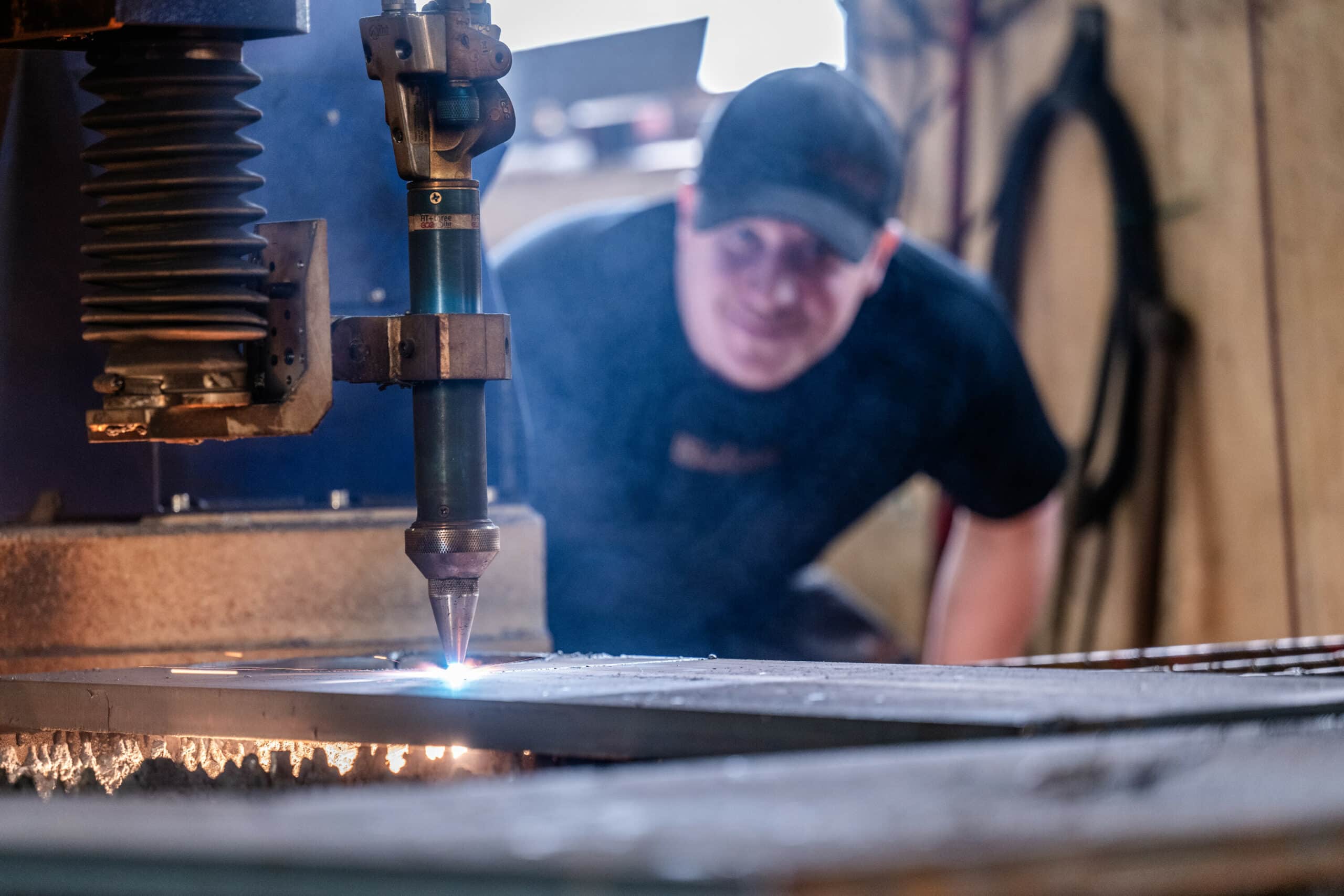 En anställd övervakar en CNC-maskin som skär i metall – gnistor och skärljus lyser upp arbetsområdet.