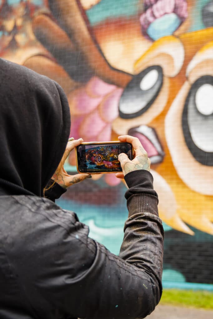 Muralmålning fotas med mobilkamera av en person med mörk jacka