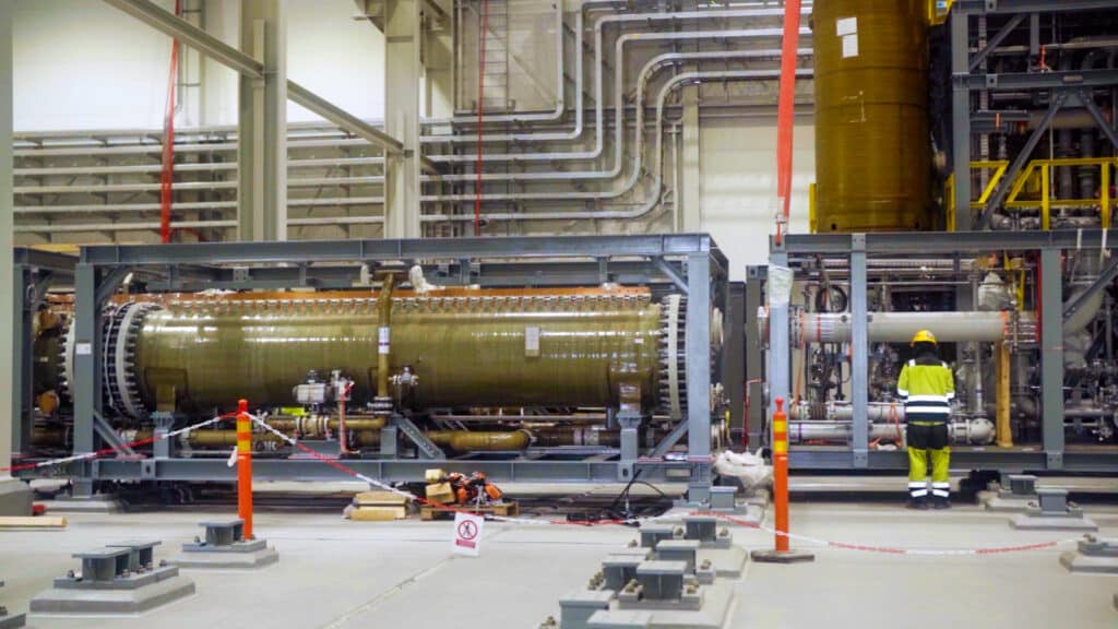 En stor elektrolysörmodul inomhus i anläggningen på Boden Industrial Park, omgiven av rörsystem och stålkonstruktioner. En arbetare i varselkläder står framför utrustningen.