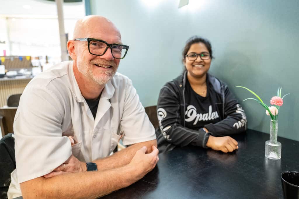 Mikael Kraus and Naveena Inavolu, sitting at a dark table with a blue-gray background