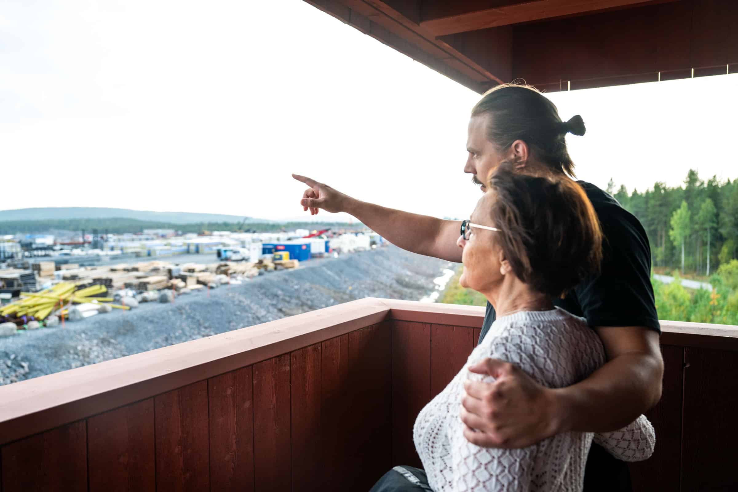 En kvinna och en man tittar ut och pekar från ett torn mot ett industriområde